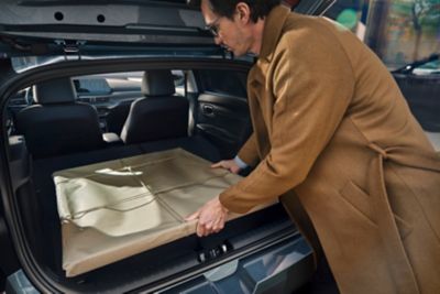 Muž v hnedom kabáte vkladá zabalený obraz do batožinového priestoru nového modelu Hyundai i20