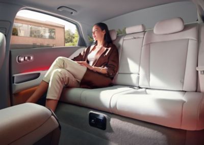 Žena sediaca na zadnom sedadle elektrického sedanu Hyundai IONIQ 6 s červeným ambientným osvetlením.