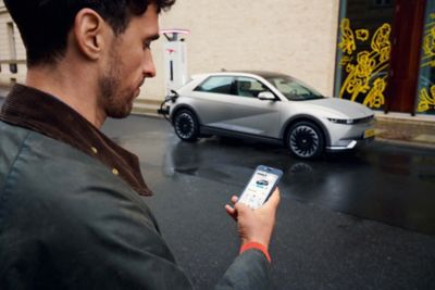 Muž prichádzajúci k elektrickému automobilu Hyundai IONIQ 5 používajúci aplikáciu Bluelink vo svojom smartfóne.