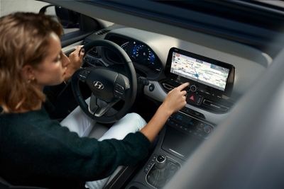 Žena sedí za volantom svojho modelu Hyundai i30 a používa dotykovú obrazovku.