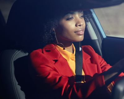 Žena uvoľnene sediaca za volantom jej modelu Hyundai KONA.