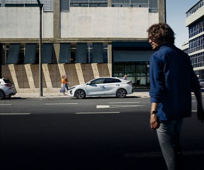 Muž prechádzajúci cez cestu k zaparkovanému vozidlu Hyundai IONIQ. V ruke drží mobilný telefón.