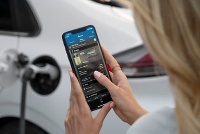 A woman checking her Hyundai IONIQ's status on her phone while charging the car.