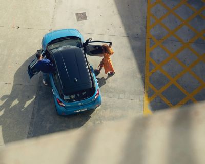 Pohľad zhora, pár nastupujúci do modrého vozidla Hyundai i10.