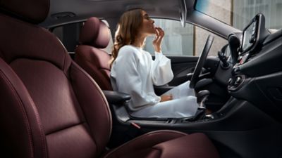 Žena sediaca na sedadle vodiča zaparkovaného modelu i30 Fastback sa pozerá do zrkadla v clone.