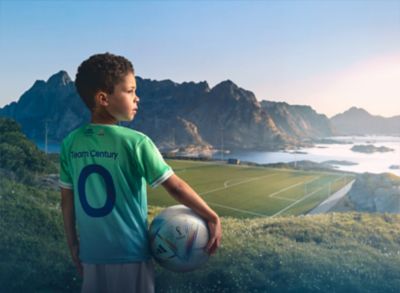 Chlapec držiaci futbalovú loptu oblečený v drese Hyundai Goal of the Century pred horami v pozadí.