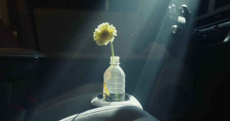 Plastová fľaša s jediným žltým kvetom umiestnená v držiaku na pohár vo vozidle Hyundai IONIQ 5, na ktorý svieti svetlo.