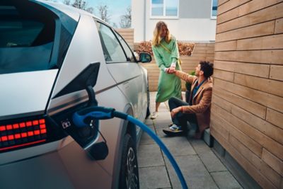 The Hyundai IONIQ 5 electric midsize CUV charging at home, a young couple sitting next to it.