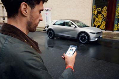 A man checking his Hyundai app while charging the Hyundai IONIQ 5 at an IONITY charging station.