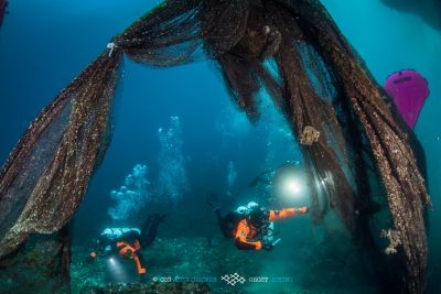 Dvaja potápači z Ghost Divers pod vodou vyťahujú vyradenú rybársku sieť na recykláciu.