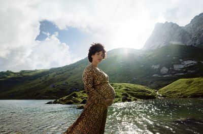 Obrázok tehotnej ženy pri alpskom jazere, pridržiavajúcej si tehotenské brucho.