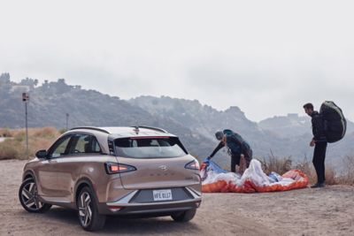 Two paragliders packing their chutes next to a Hyundai NEXO hydrogen fuel cell vehicle.
